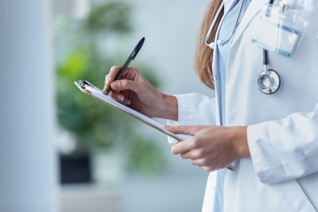Female doctor filling up medical form at clipboard while standin